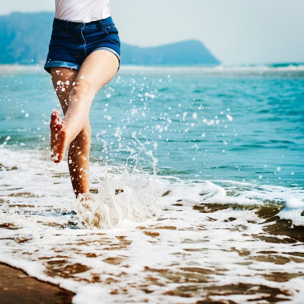 Body Typed: Woman walking barefoot on beach, ocean waves splashing. Beach and Body Type concept.