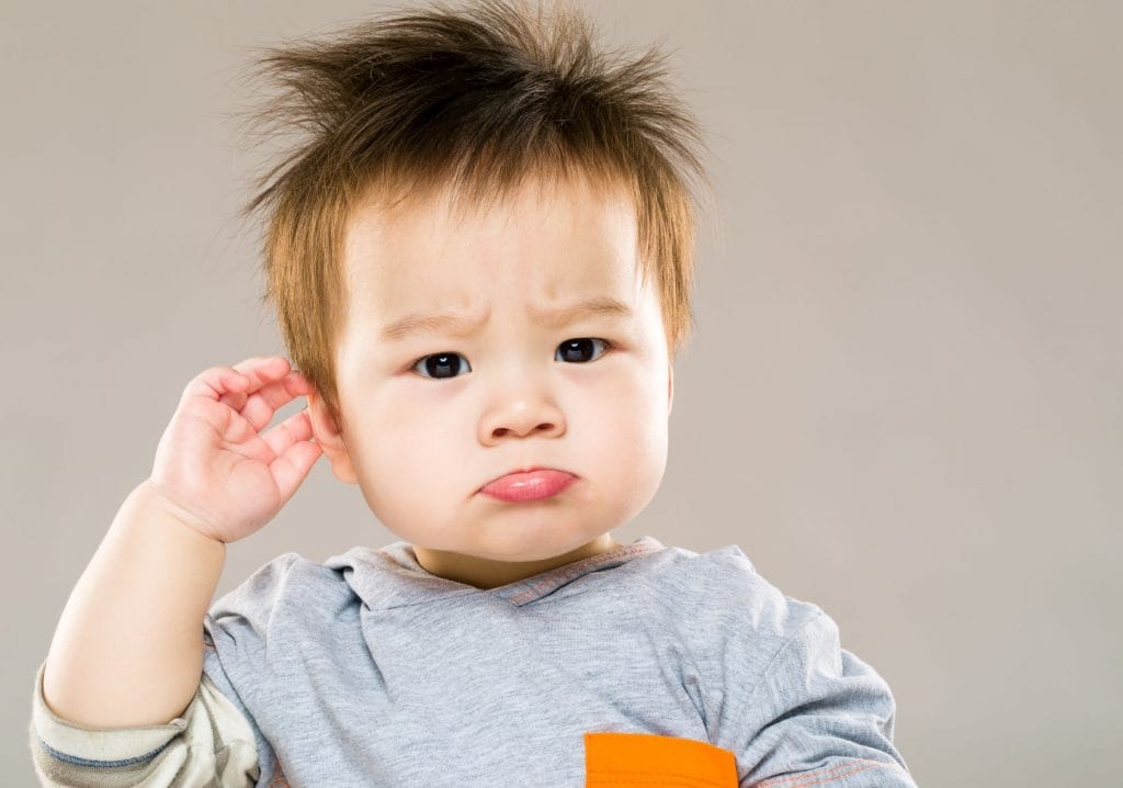 Worried toddler touching ear, a common sign of childhood ear infection.