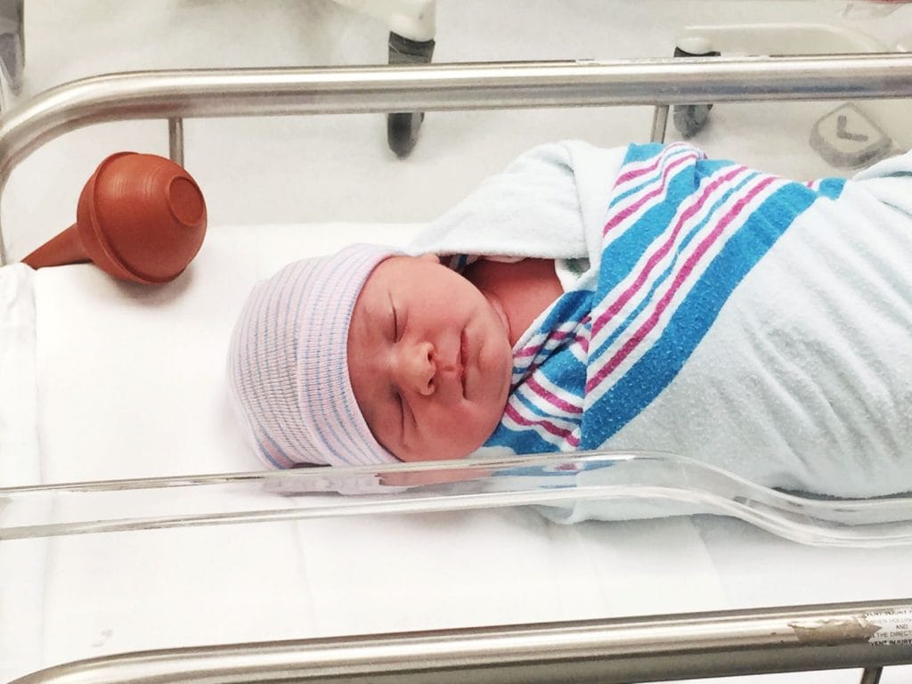 Newborn baby sleeping peacefully in hospital bassinet, wrapped in blanket and wearing a striped hat. A Perfect Day.