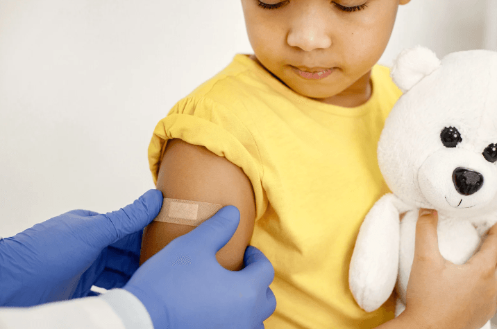 Child getting vaccine with teddy bear. Pediatric care for holistic health and plant-based options.
