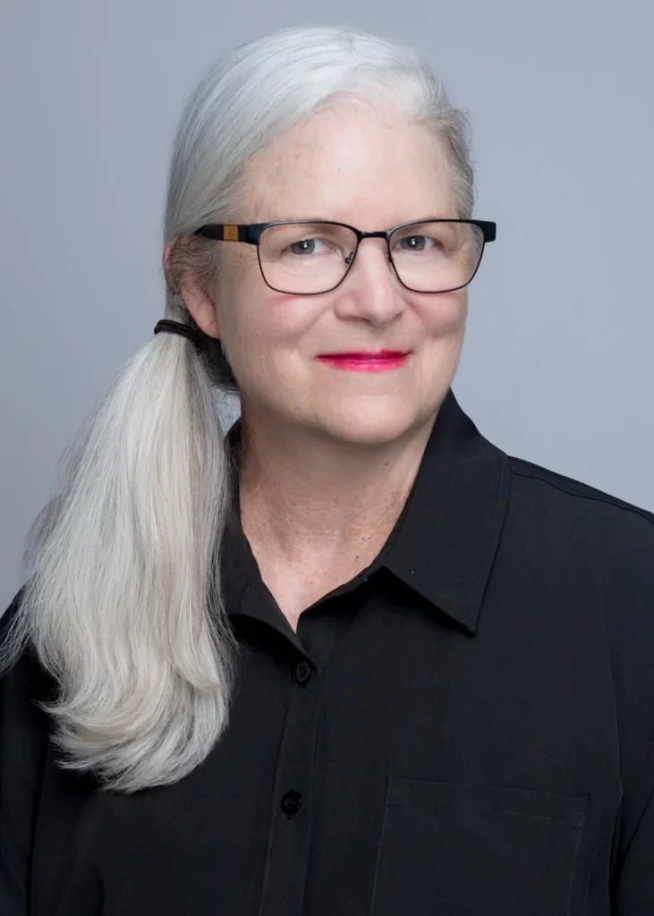 Cornelia Franz portrait. Woman with gray hair, glasses, and a black shirt smiles at the camera for her Home page profile.