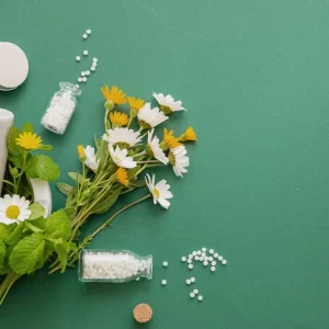 Homeopathy globules, herbs, mortar and pestle on green background for natural medicine concept.