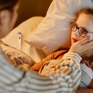 Sick daughter with fever in bed, part of herbaceutical kit. Caregiver checking her temperature. Herbal remedies for kids.