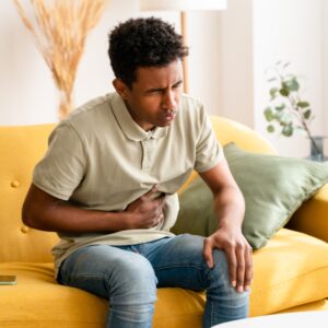 GI Bundle: Man on sofa with upset stomach, experiencing abdominal pain and discomfort. Digestive health concept.