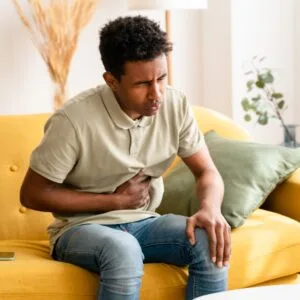 GI Bundle: Man on sofa with upset stomach, experiencing abdominal pain and discomfort. Digestive health concept.